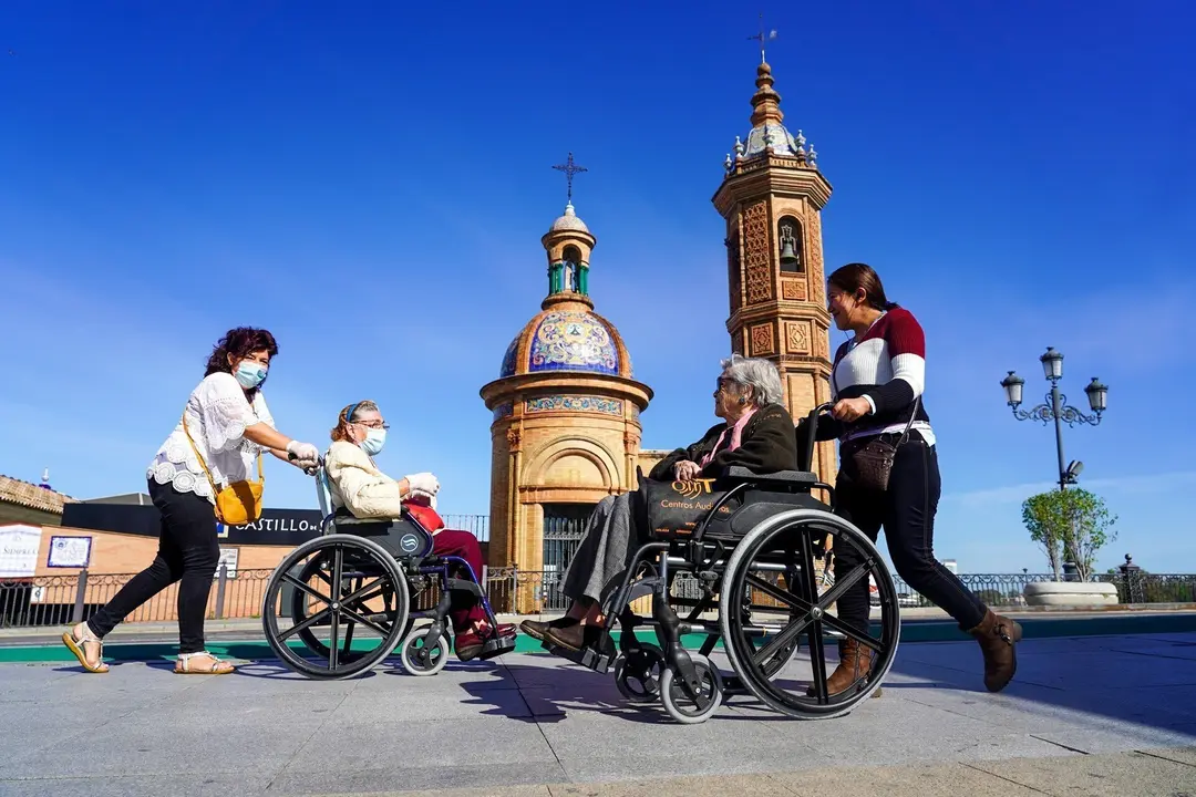 Dos personas mayores en silla de ruedas se saludan a la entrada del Puente de Triana, en Sevilla (Andaluc&iacute;a, Espa&ntilde;a).