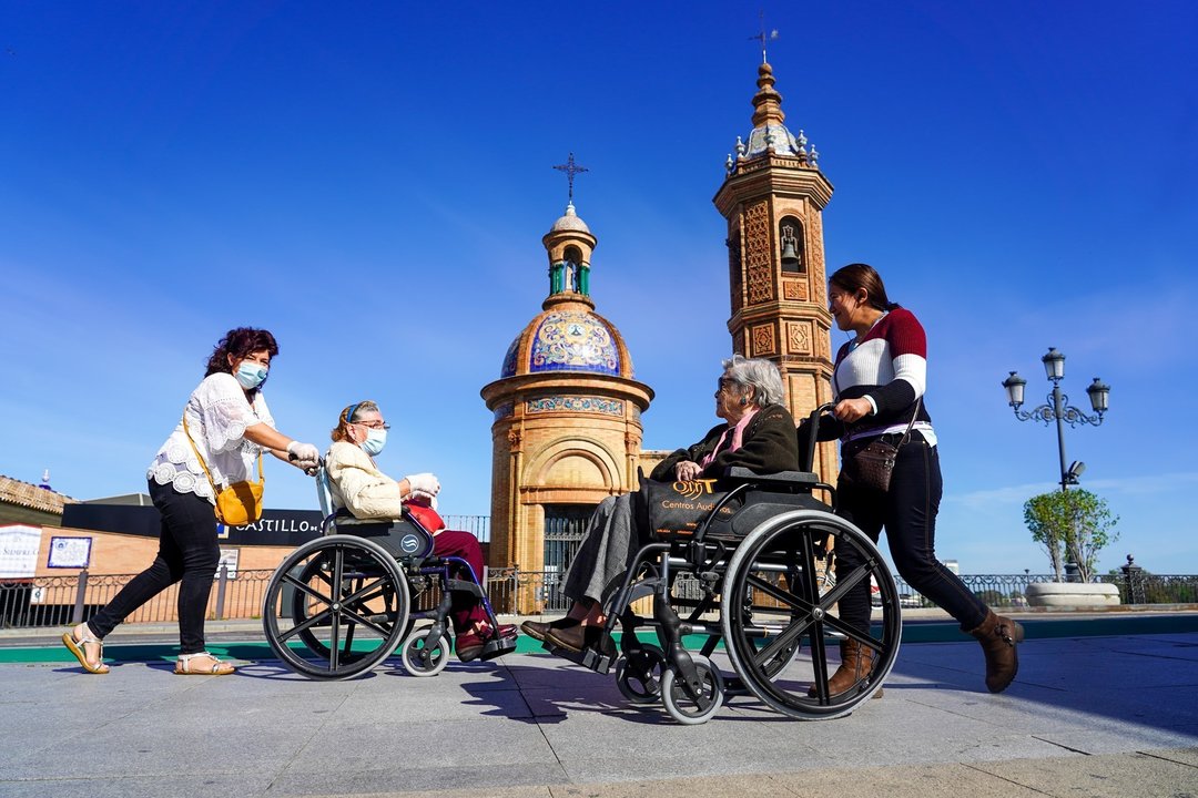 Dos personas mayores en silla de ruedas se saludan a la entrada del Puente de Triana, en Sevilla (Andalucía, España).