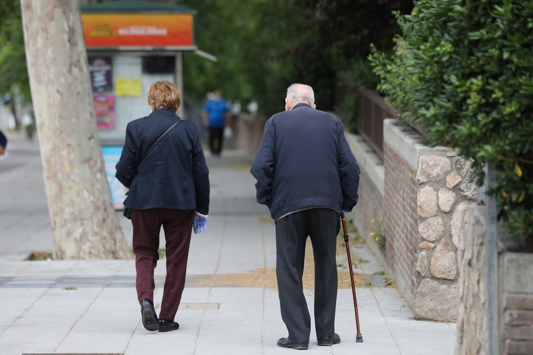 Una mujer y un hombre con bastón pasean por Madrid.