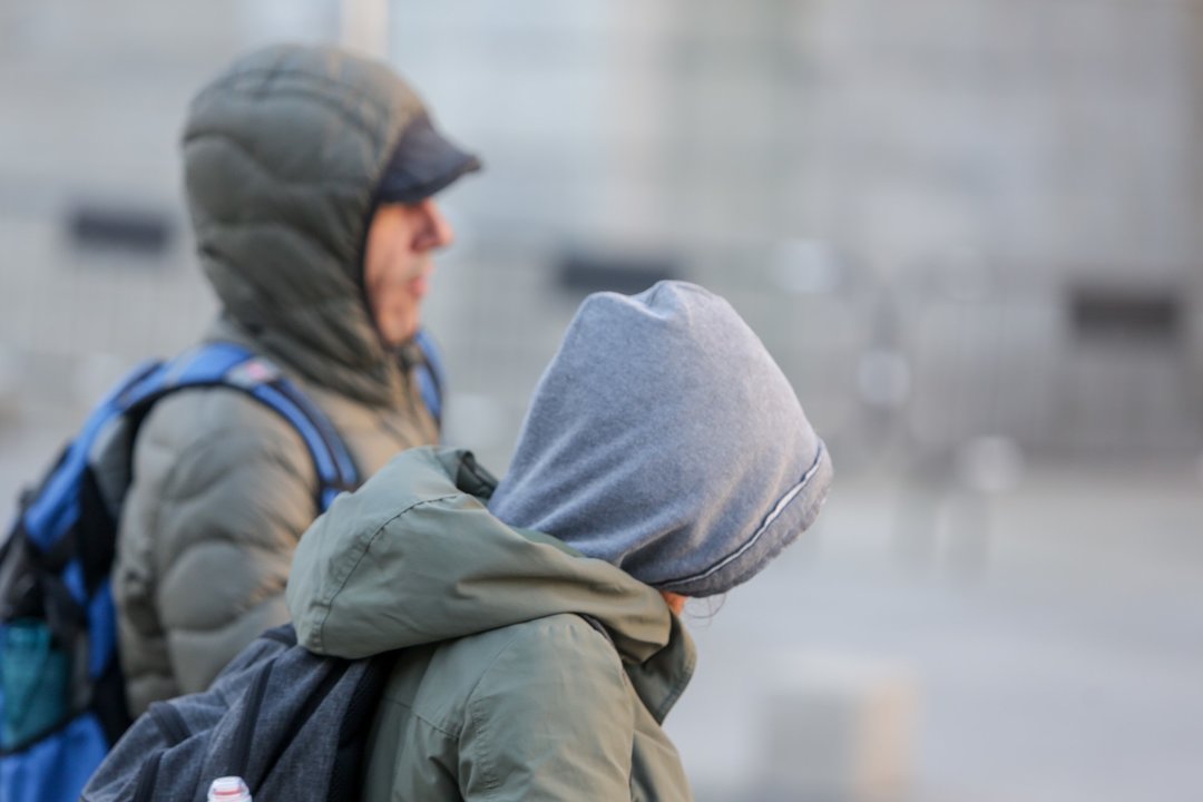 Dos jovenes se protegen del frío con abrigos y gorros mientras pasean durante un día de frío y viento por Madrid