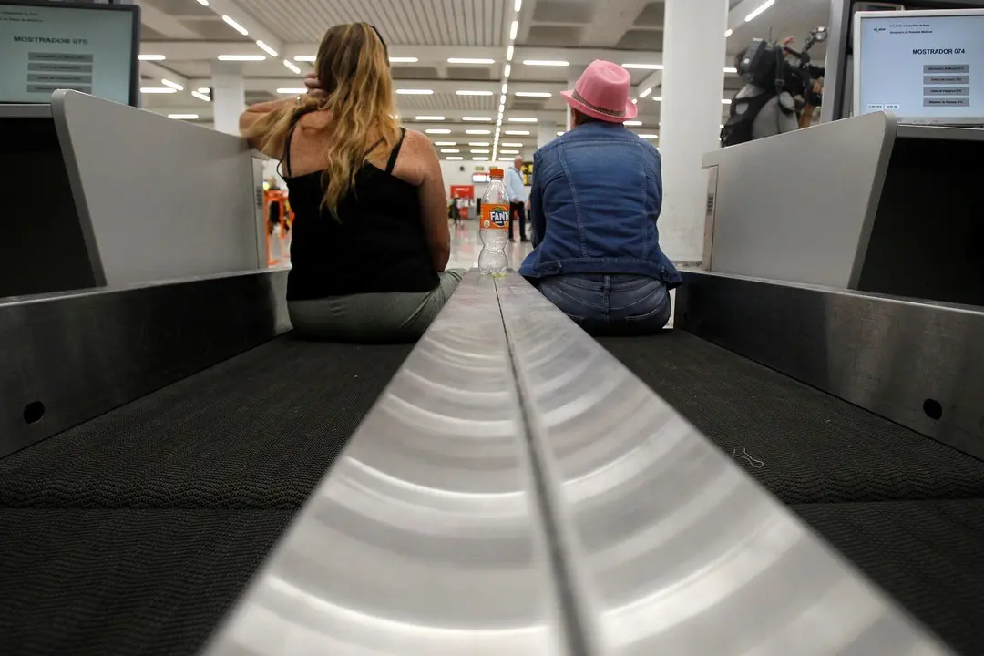 Dos turistas esperan sentadas en una cinta transportadora de maletas en el aeropuerto de Palma de Mallorca (Baleares), horas despu&eacute;s de que la compa&ntilde;&iacute;a brit&aacute;nica Thomas Cook anunciase su quiebra y de que varios de sus vuelos fuesen cancelados, a 23 de sep