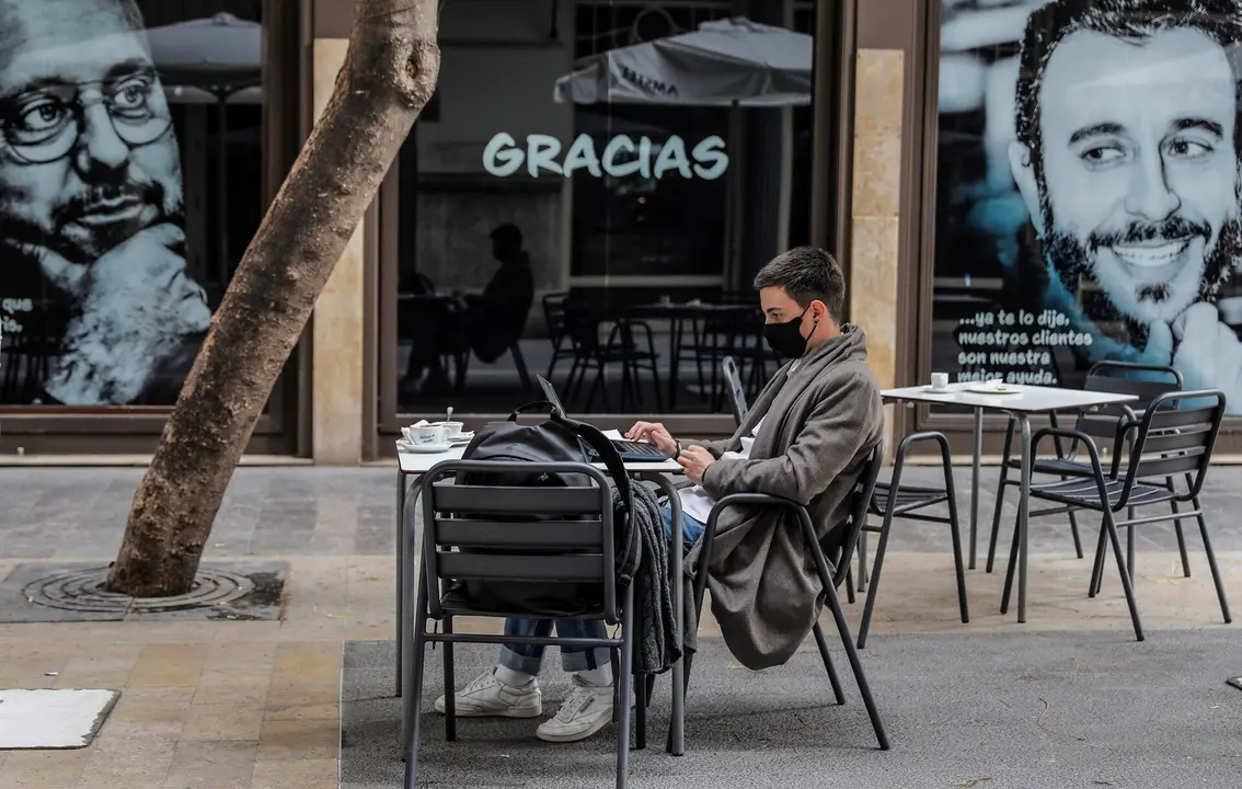 Un joven trabaja con su ordenador port&aacute;til en una terraza el primer d&iacute;a de la apertura de la hosteler&iacute;a en Valencia, Comunidad Valenciana (Espa&ntilde;a), a 1 de marzo de 2021. Coincidiendo con el inicio de la desescalada en la regi&oacute;n, la hosteler&iacute;a de la Comuni