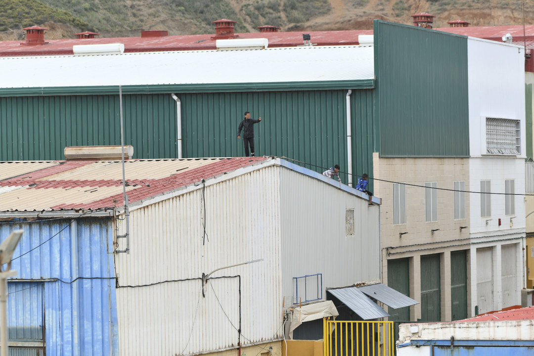 Varios niños caminan por un tejado al tratar de escapar de la nave de primera acogida del polígono del Tarajal, en Ceuta.