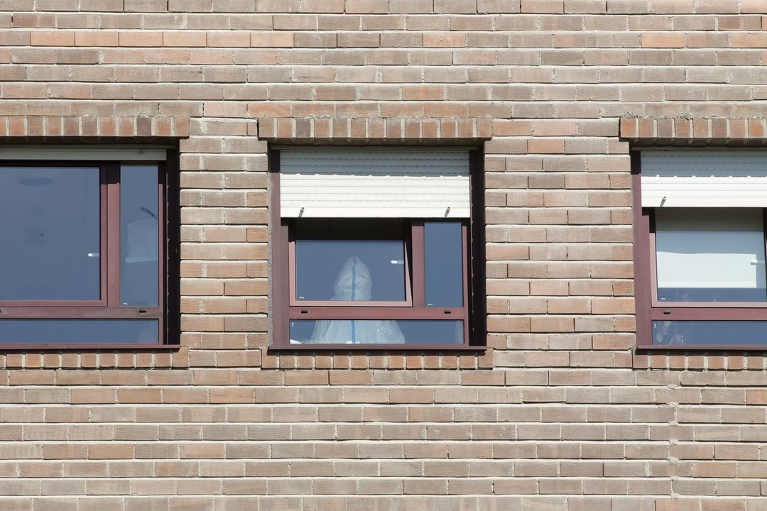Un trabajador sanitario con un EPI en la ventana de una habitación de una residencia