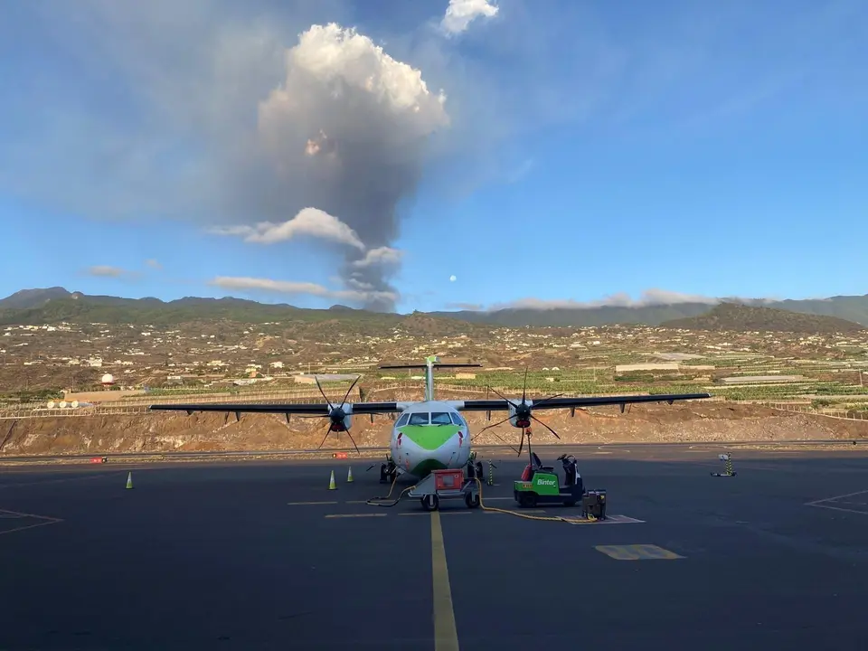 Un avi&oacute;n de Binter en la pista del aeropuerto de La Palma, con el volc&aacute;n en erupci&oacute;n al fondo
