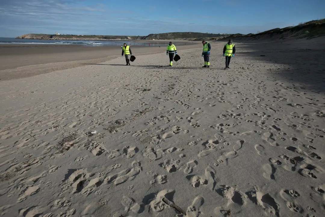 Operarios de la empresa TRAGSA realizan labores de recogida de "pellets" en la playa de Salinas. En Castrill&oacute;n (Asturias), a 13/01/2023 (&copy; Jorge Peteiro / Europa Press)