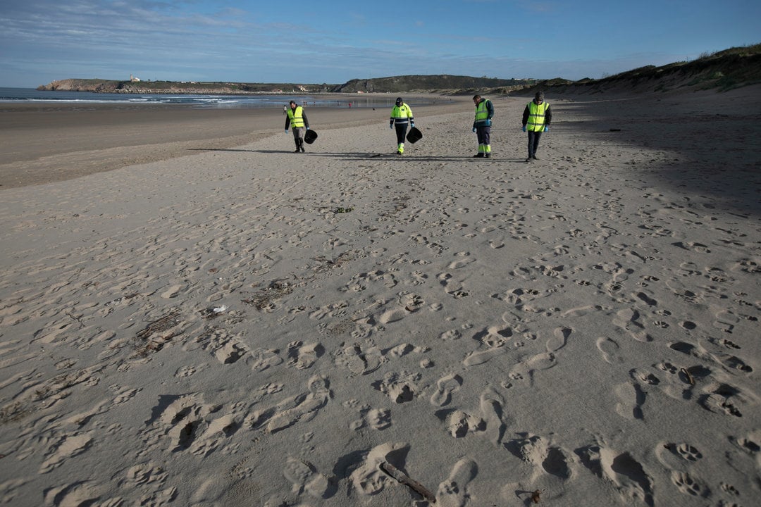 Operarios de la empresa TRAGSA realizan labores de recogida de "pellets" en la playa de Salinas. En Castrillón (Asturias), a 13/01/2023 (© Jorge Peteiro / Europa Press)