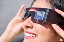 Smiling young latin woman watching an eclipse of the sun with eclipse glasses