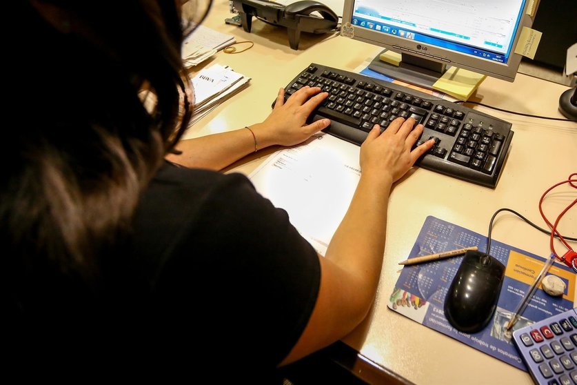 Una mujer escribe en el teclado de su ordenador, en el despacho de la oficina.