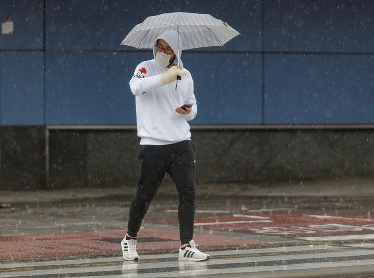 Transeúntes protegidos con mascarilla y un paraguas caminan por las calles de la capital un día marcado por la llegada a la península de una borrasca fría que ha activado la alerta por viento o lluvia en 8 comunidades, entre ellas, Madrid, en los inicios 
