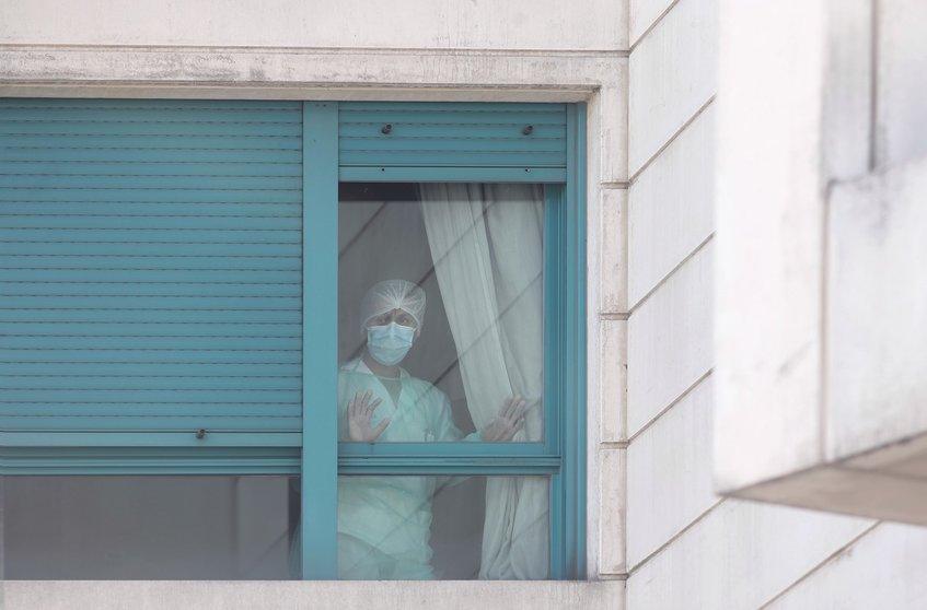 Archivo - Una trabajadora del personal sanitario protegida con mascarilla se asoma por una de las ventanas de una residencia de Madrid.