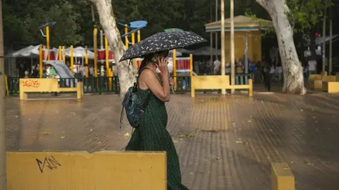 Mujer habla por el m&oacute;vil mientras camina bajo su parag&uuml;as.