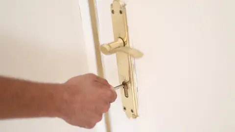 Un hombre introduce una llave en la cerradura de la puerta de una vivienda.