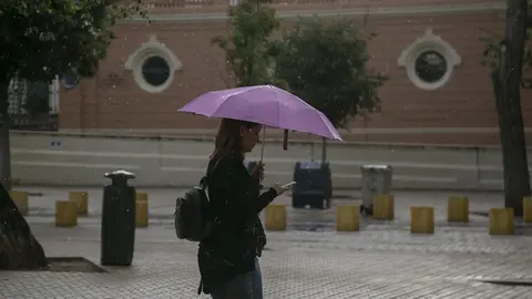 Una mujer se protege de la lluvia bajo su parag&uuml;as mientras camina. Sevilla.