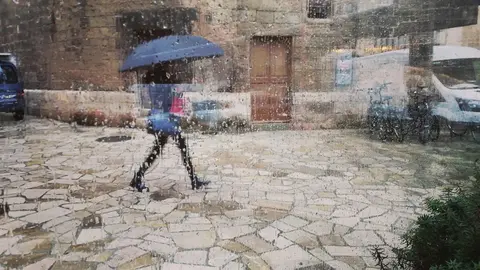 Una mujer pasea por el centro de Palma con un paraguas, vista a trav&eacute;s de un cristal con gotas de lluvia.