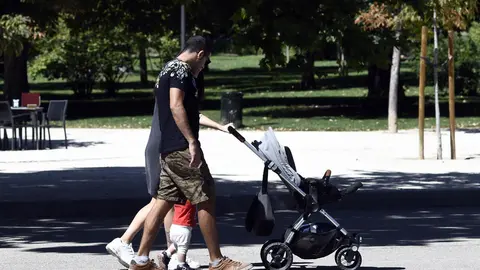 Una pareja y su beb&eacute; empujan el carrito del mismo en un parque de Madrid.