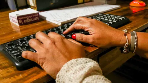 Unas manos de mujer escriben en el teclado de un ordenador, sobre una mesa de madera.