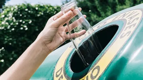 Una mujer reciclando un residuo de envase de vidrio en el contenedor verde