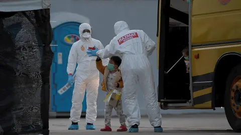 Trabajadores con trajes de protecci&oacute;n ayudan a un ni&ntilde;o en un minub&uacute;s en Malasia