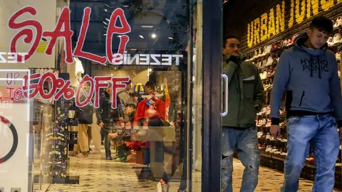 Dos hombres salen de una tienda de zapatos en Madrid, donde se ofertan rebajas de hasta el 50%.