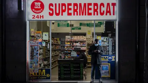 Un hombre protegido con una mascarilla en la puerta de un supermercado 24 horas abierto durante el primer d&iacute;a laborable de la segunda semana desde que se decret&oacute; el estado de alarma en el pa&iacute;s a consecuencia del coronavirus, en Barcelona/Catalunya (Espa&ntilde;a