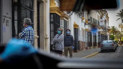 Personas hacen cola para acceder al banco durante el per&iacute;odo de confinamiento en el estado de alarma por coronavirus, covid-19. En Arahal, Sevilla (Andaluc&iacute;a, Espa&ntilde;a), a 25 de marzo de 2020.