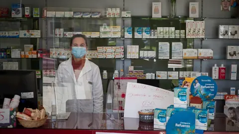 Una farmac&eacute;utica contin&uacute;a trabajando protegida por una m&aacute;scara sanitaria y una mampara.