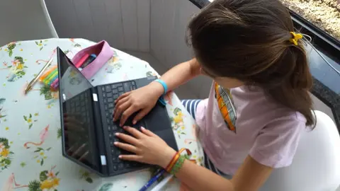 Una ni&ntilde;a, haciendo deberes en casa con el ordenador port&aacute;til.