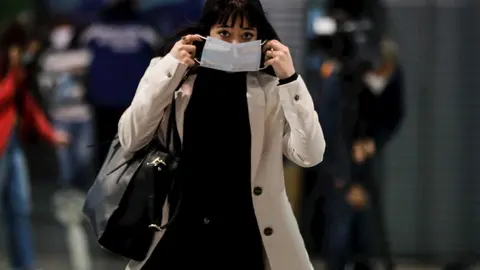 Una pasajera se coloca la mascarilla que previamente le han proporcionado Agentes de la Polic&iacute;a Municipal de Madrid en el intercambiador de la estaci&oacute;n Puerta de Atocha, en Madrid (Espa&ntilde;a), a 13 de abril de 2020.