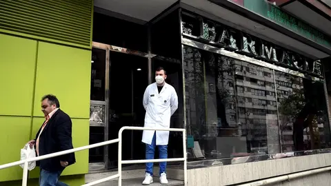 Un farmac&eacute;utico protegido con mascarilla en la puerta de una Farmacia