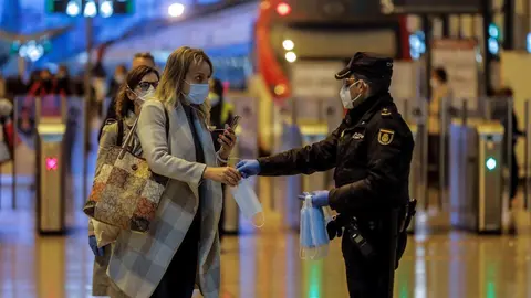 Un polic&iacute;a nacional entrega una mascarilla a una mujer en el vest&iacute;bulo de la estaci&oacute;n del Norte de Valencia el d&iacute;a en el que se reactiva la actividad laboral no esencial en las empresas cuyos empleados no puedan teletrabajar