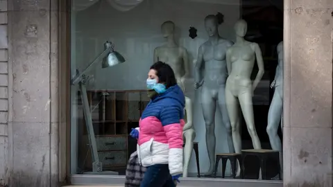 Una mujer protegida con una mascarilla pasa junto a un escaparate de una tienda cerrada. Archivo