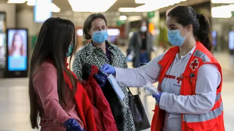 Voluntarios de Cruz Roja entregan mascarillas a pasajeros en la estaci&oacute;n de Cercan&iacute;as de Atocha, en Madrid