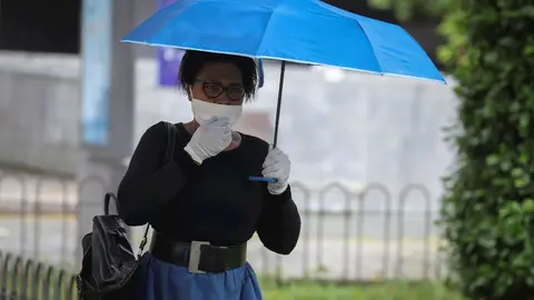 Una mujer protegida con mascarilla y guantes se resguarda de la lluvia bajo su parag&uuml;as en la quinta semana del estado de alarma por el coronavirus, Covid-19. En Sevilla (Andaluc&iacute;a, Espa&ntilde;a), a 15 de abril 2020.