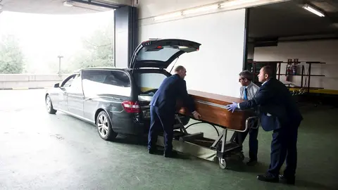 Trabajadores de servicios funerarios introducen un f&eacute;retro en el veh&iacute;culo 