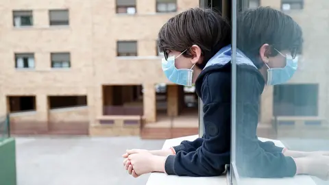 Un ni&ntilde;o con una mascarilla se asoma a la ventana de su casa durante el confinamiento
