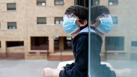 Un ni&ntilde;o con una mascarilla se asoma a la ventana de su casa durante el confinamiento por el coronavirus, en Valdemoro/Madrid (Espa&ntilde;a) a 20 de abril de 2020.