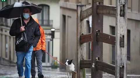 Un hombre con mascarilla camina bajo la lluvia junto al vallado permanente del encierro de Pamplona de la cuesta de Santo Domingo