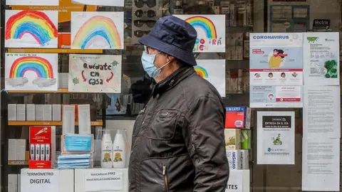 Un hombre con mascarilla pasa junto a una farmacia con dibujos infantiles en su escaparate .
