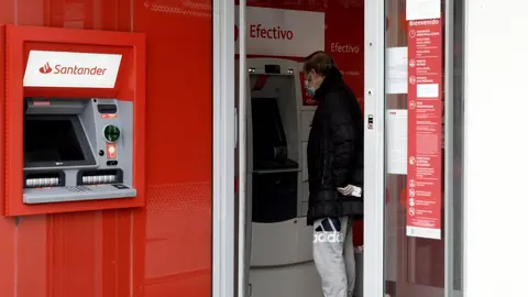 Un hombre saca dinero de un cajero del Banco Santander.