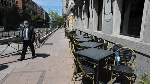 Un hombre con mascarilla pasa junto a una terraza cerrada de un bar 
