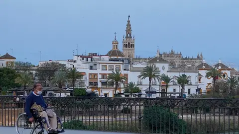 Un ciudadano en silla de ruedas por el Puente de Triana casi des&eacute;rtico a los 40 d&iacute;as de estado de alarma en Sevilla a 23 abril del 2020