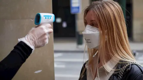 Una trabajadora de la tienda de moda Urban Sons le toma la temperatura a una clienta