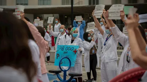 Decenas de miembros del personal sanitario protegidos con mascarilla sostienen carteles durante la concentraci&oacute;n de sanitarios en el D&iacute;a Internacional de la Enfermer&iacute;a a las puertas del Hospital Vall d'Hebron. En Barcelona, a 12 de mayo de 2020.