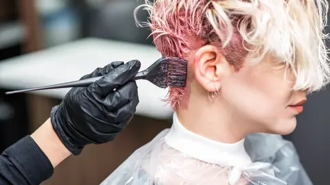 The professional hairdresser uses a brush to apply the pink dye to the hair. Hair coloring concept.