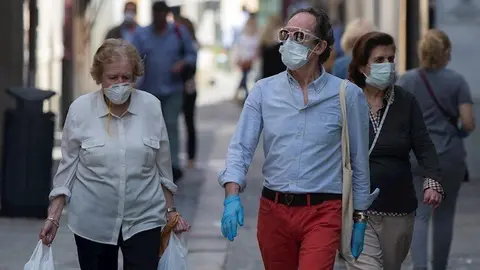 Varias personas caminan protegidas con mascarillas por una calle del centro de la ciudad, tras el nuevo acuerdo de Gobierno en el cual el uso de mascarillas ser&aacute; obligatorio tambi&eacute;n en la v&iacute;a p&uacute;blica y en espacios cerrados cuando no se pueda garantizar el