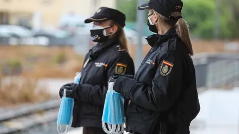 Polic&iacute;as nacionales se preparan para entregar mascarillas a los viajeros que esperan en un and&eacute;n durante el estado de alarma