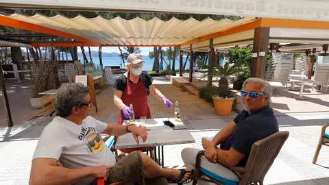 20 May 2020, Spain, Calvia: A waitress serves beer to customers at the "Essbar" restaurant terrace on the beach of Paguera on the Spanish island of Mallorca. Some Spanish provinces have been allowed to relax the first blocking measures in a first phase si