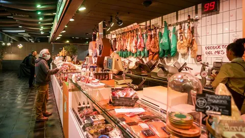 Varios clientes hacen la compra en un puesto de carne y embutidos en el mercado de San Ant&oacute;n, que permanece abierto y anuncia que tambi&eacute;n atiende a domicilio, en Madrid (Espa&ntilde;a), a 18 de marzo de 2020.