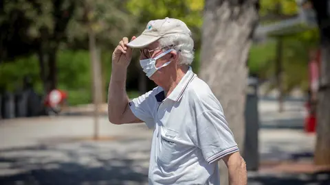 Un hombre con mascarilla y gafas de sol se coloca una gorra